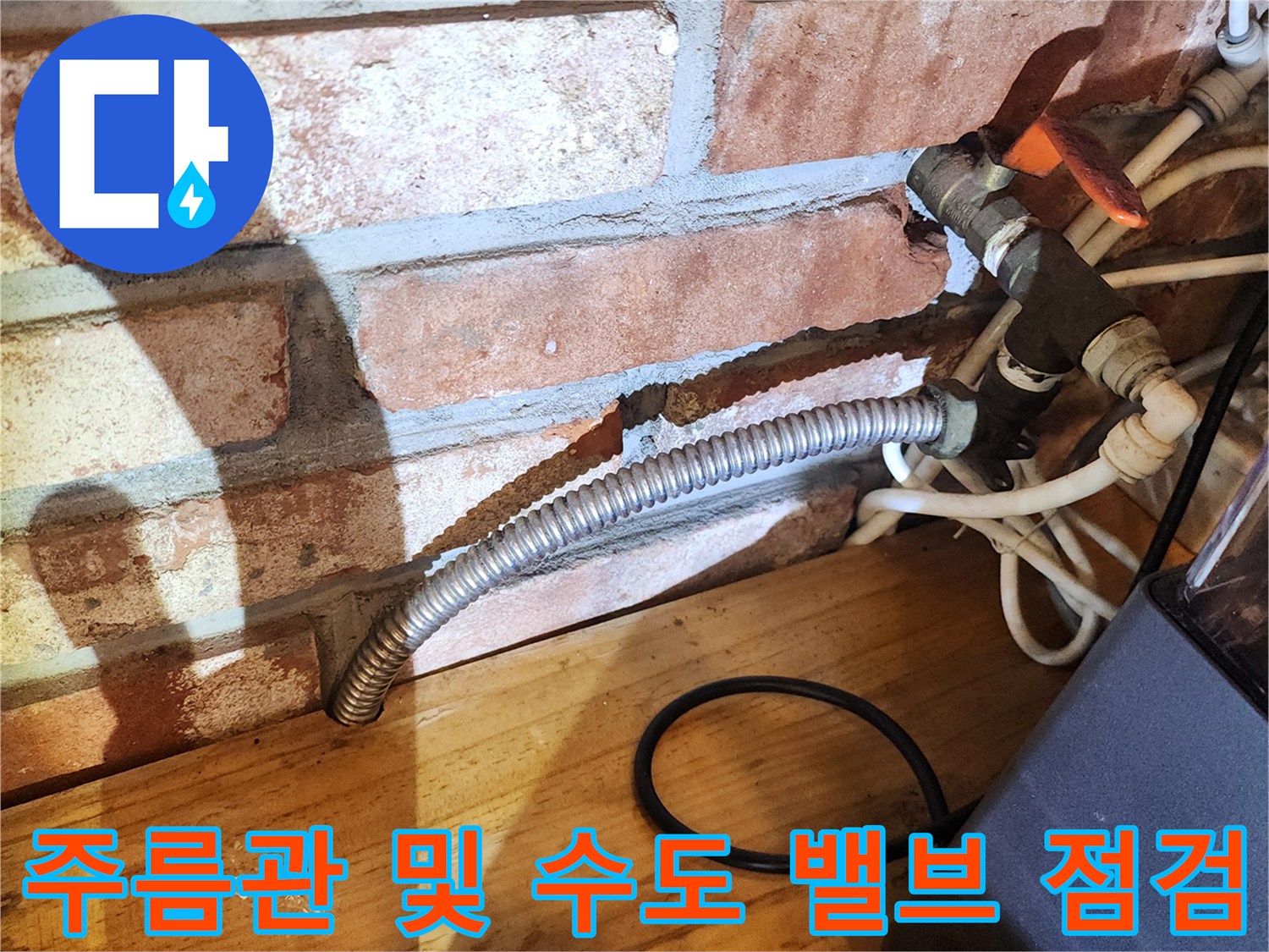 싱크대 아래쪽-노출된 금속 주름관과 벽돌 벽면의 모습