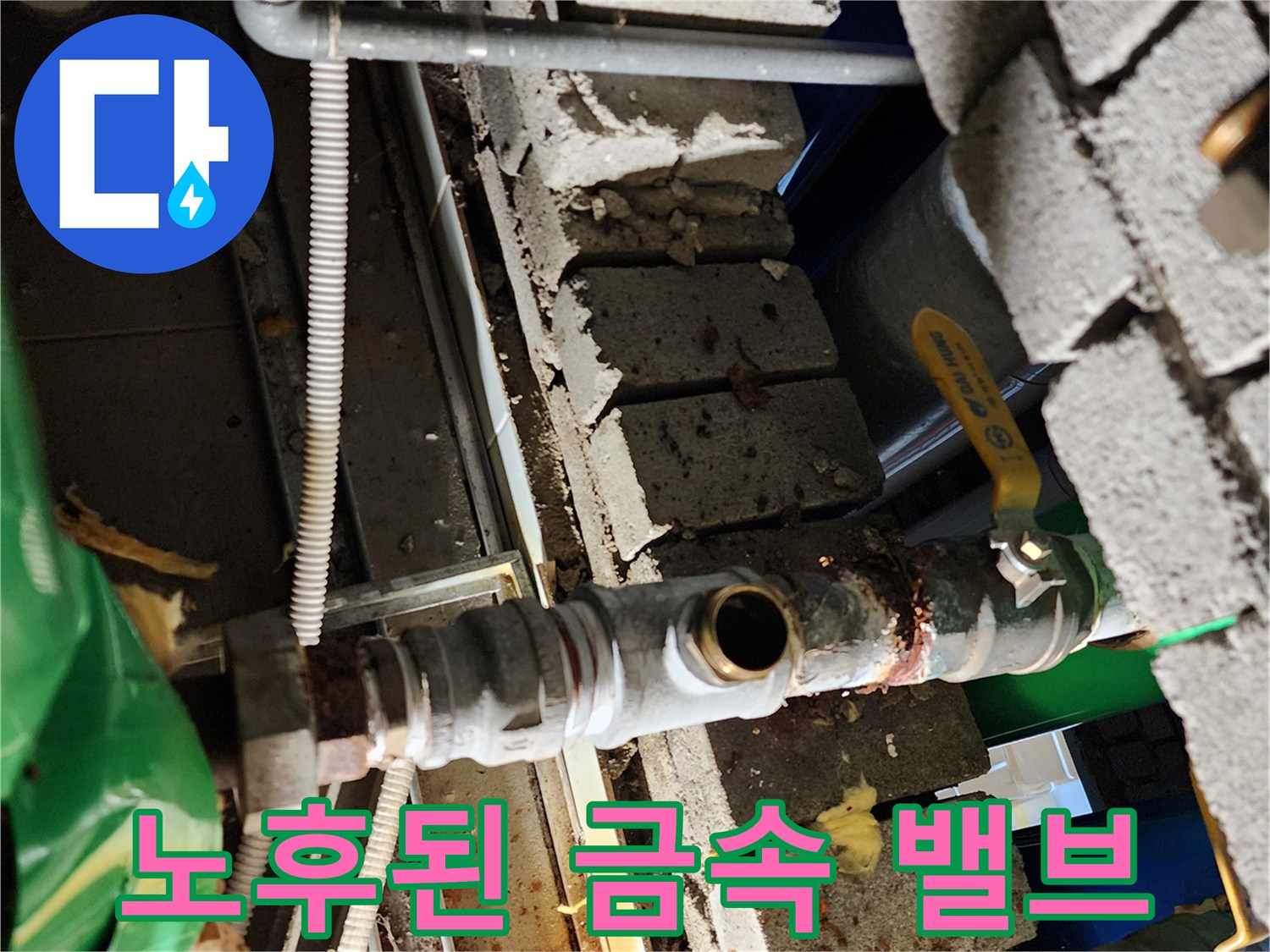 벽돌 틈새에 설치된 녹슨 금속 배관과 노란색 손잡이 밸브입니다.