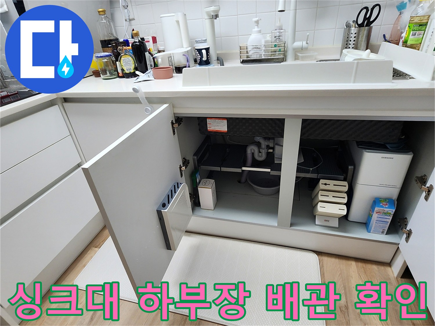 주방 싱크대 하부장 내부의 배관과 분배기 연결 상태를 점검하는 모습