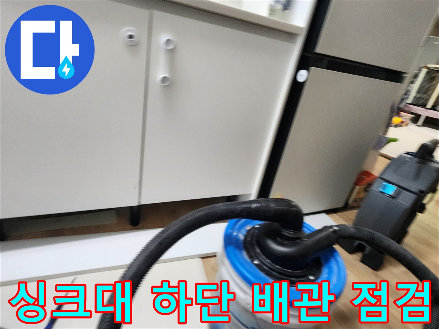주방 싱크대 하부장 아래 배관과 청소용 장비가 놓여 있는 모습