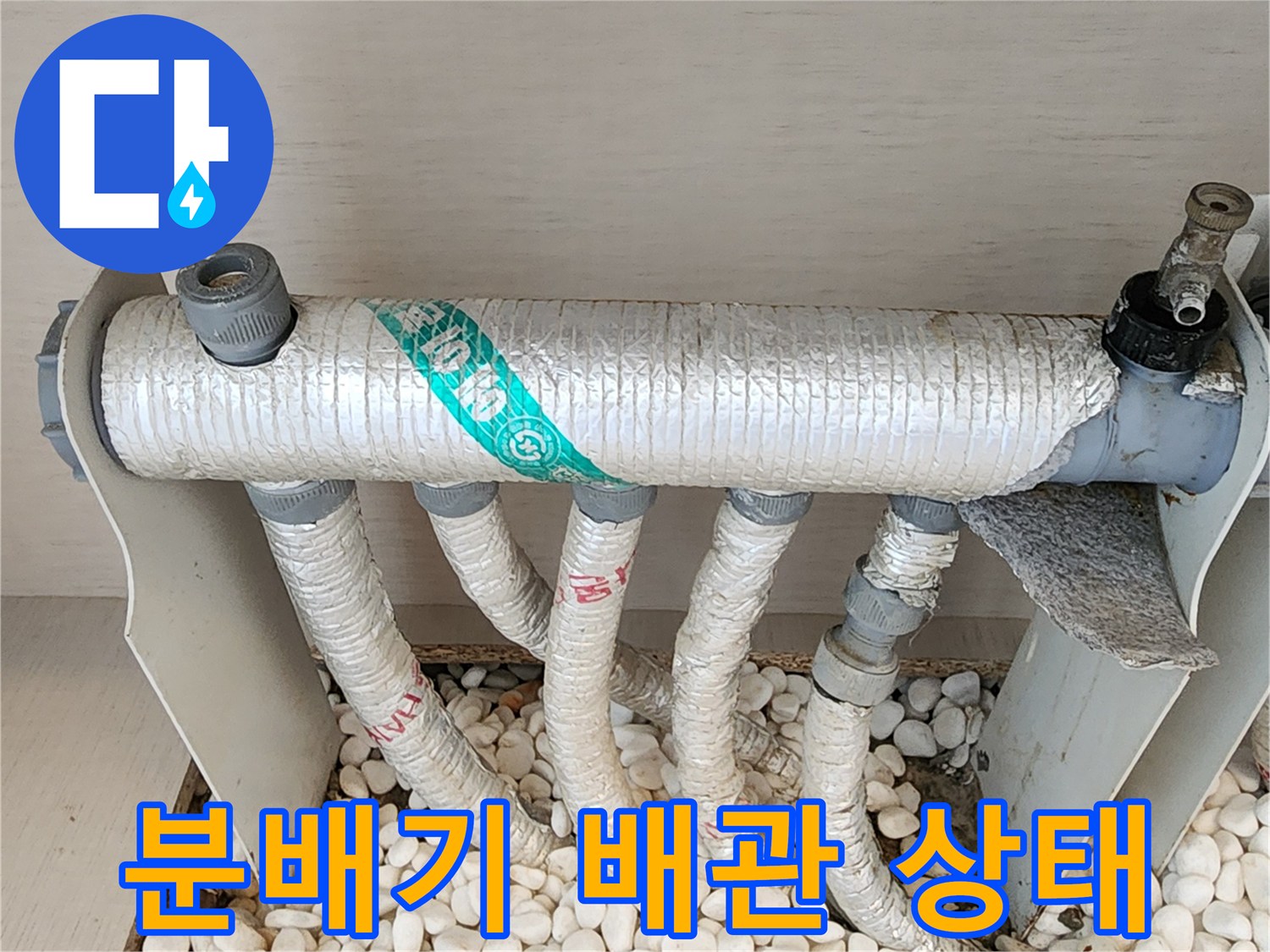 흰색 자갈로 덮인 분배기-보온재가 감싸진 배관 연결부