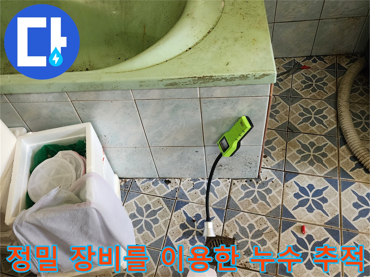 초록색 휴대용 가스 탐지기가 욕실 바닥 근처에서 배관 누수를 감지하고 있습니다.