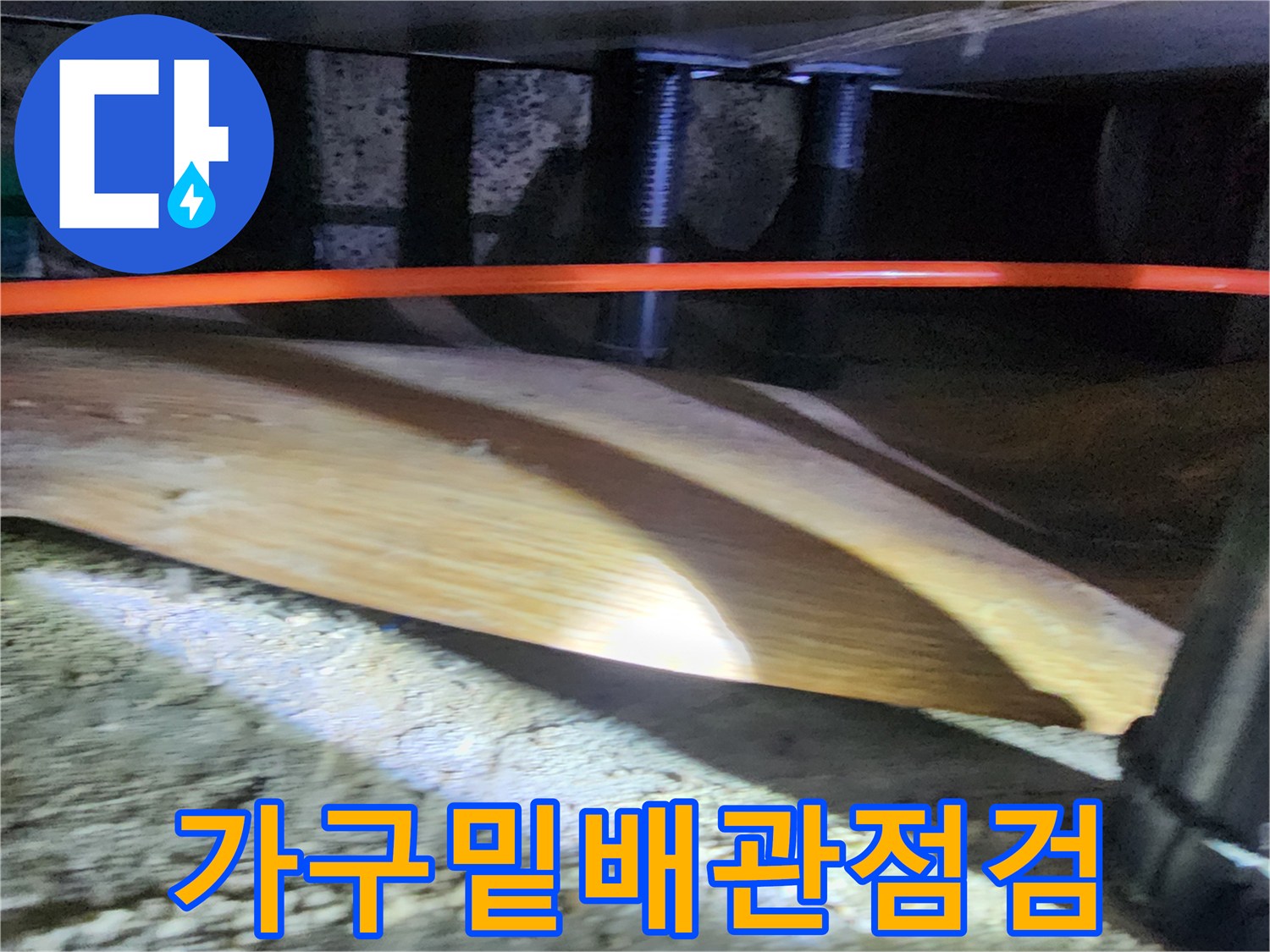 가구 아래 좁은 공간에 위치한 주황색 배관과 습기 흔적