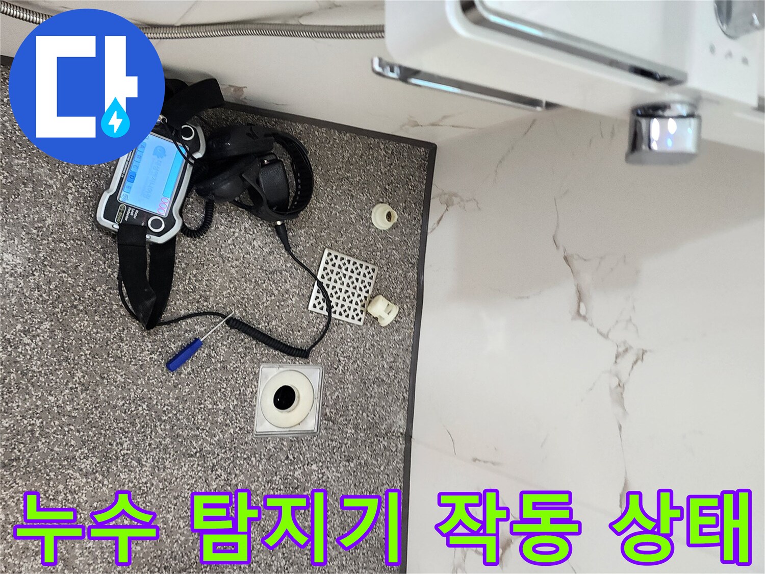 욕실 바닥에 놓인 가스식 누수 탐지 장비와 배수구 부품