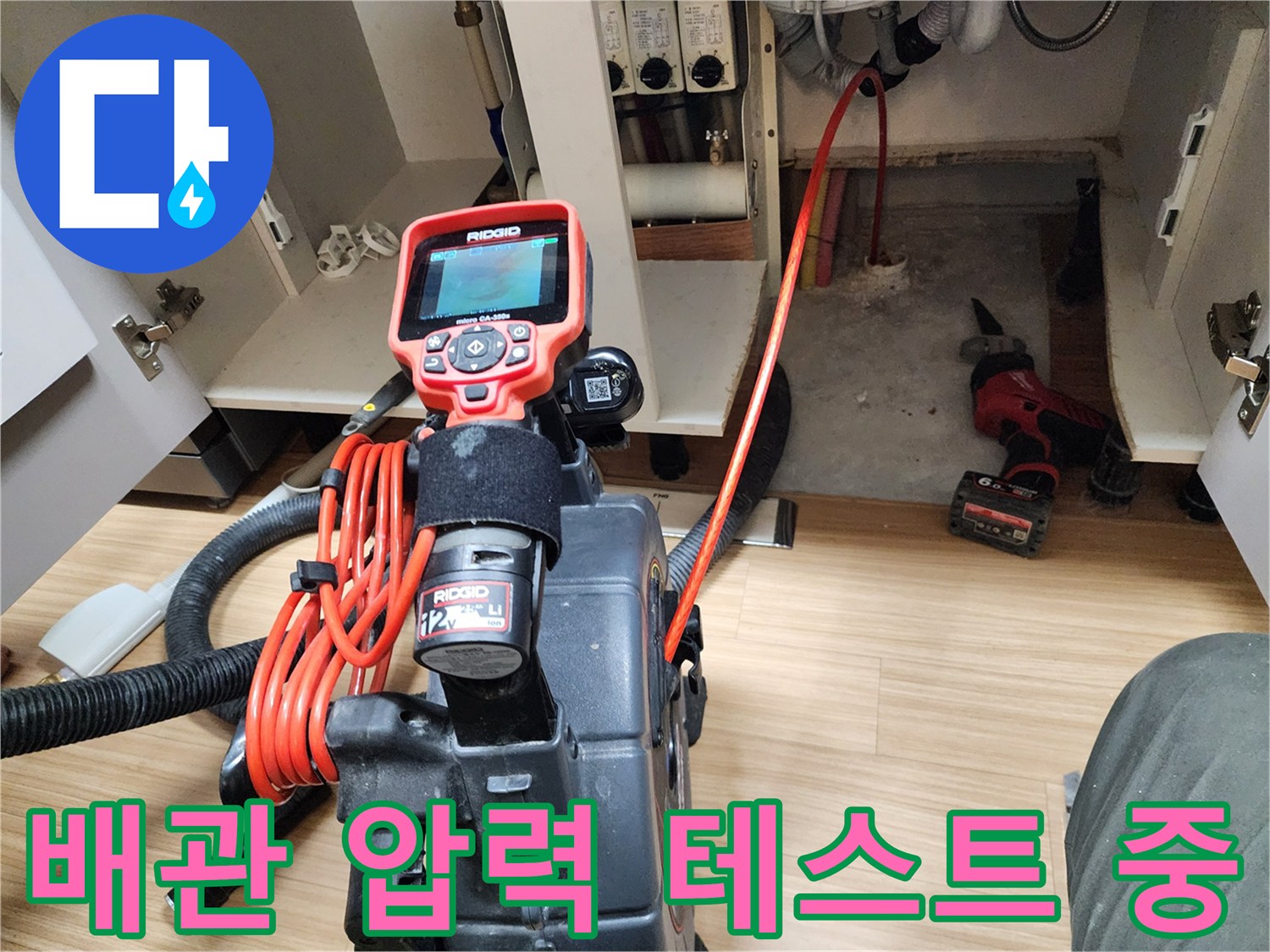 싱크대 하부장 내부에서 배관의 기밀성을 확인하기 위해 공압 테스트기를 연결한 모습입니다.