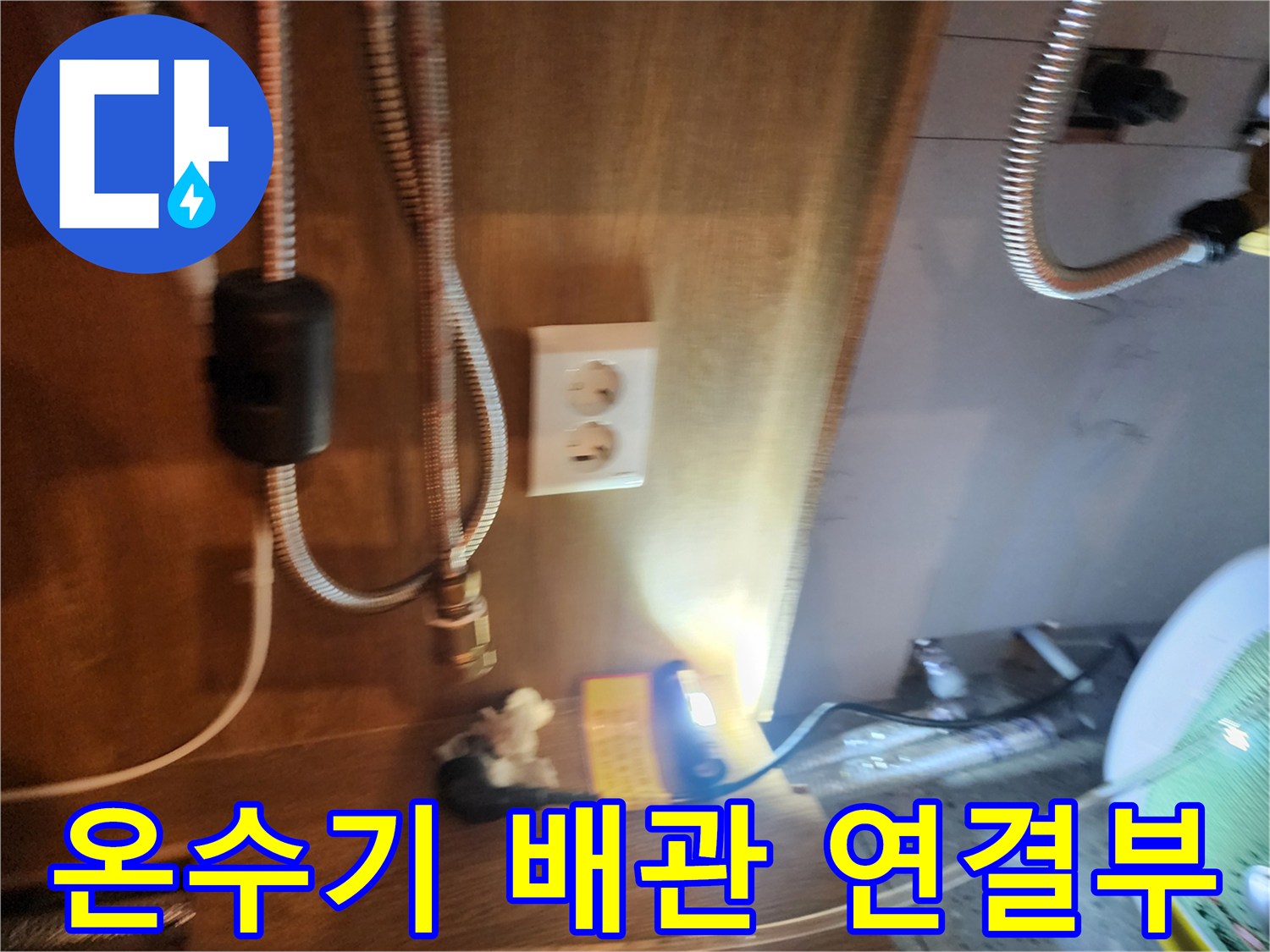 주방 하부장 내 설치된 전기 온수기와 금속 호스 연결 부위 모습