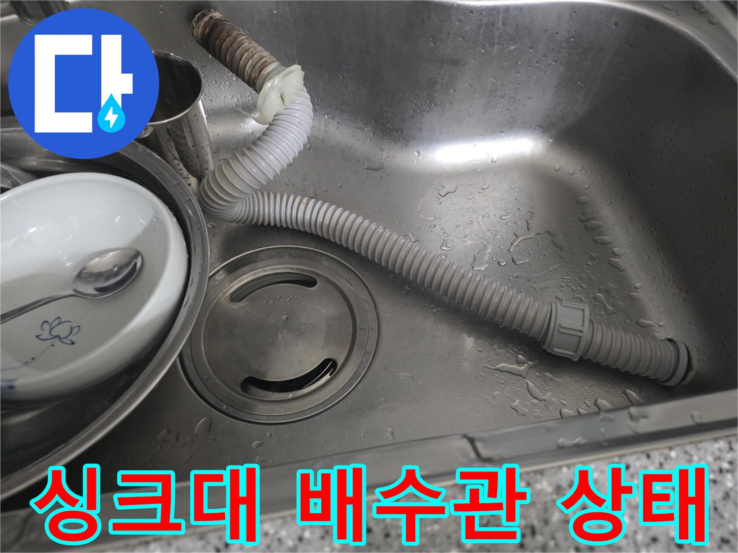 스테인리스 싱크볼 내부에 놓인 회색 주름 배관과 배수구 모습