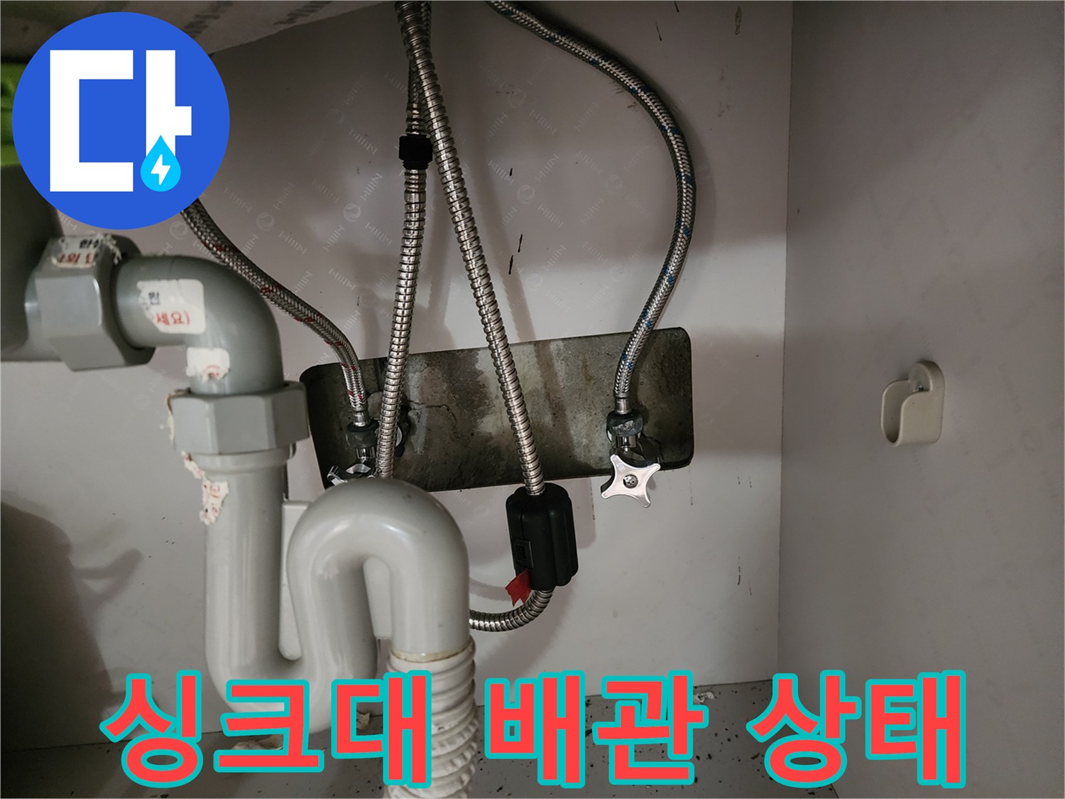싱크대 하부장 내부의 금속 자바라 호스와 수도 밸브 모습