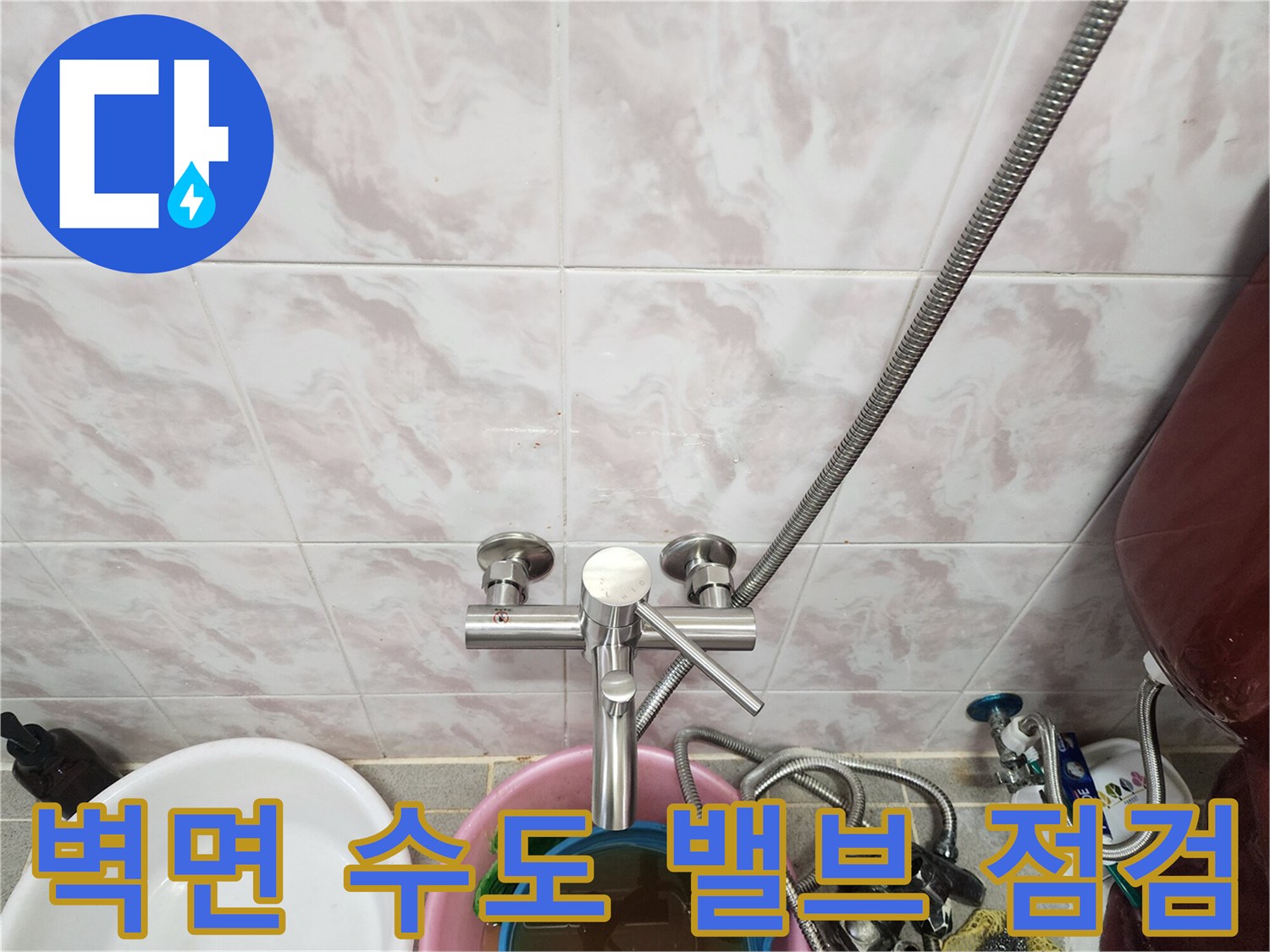 타일 벽면에 고정된 은색 수도 부속과 연결 호스 상세 모습