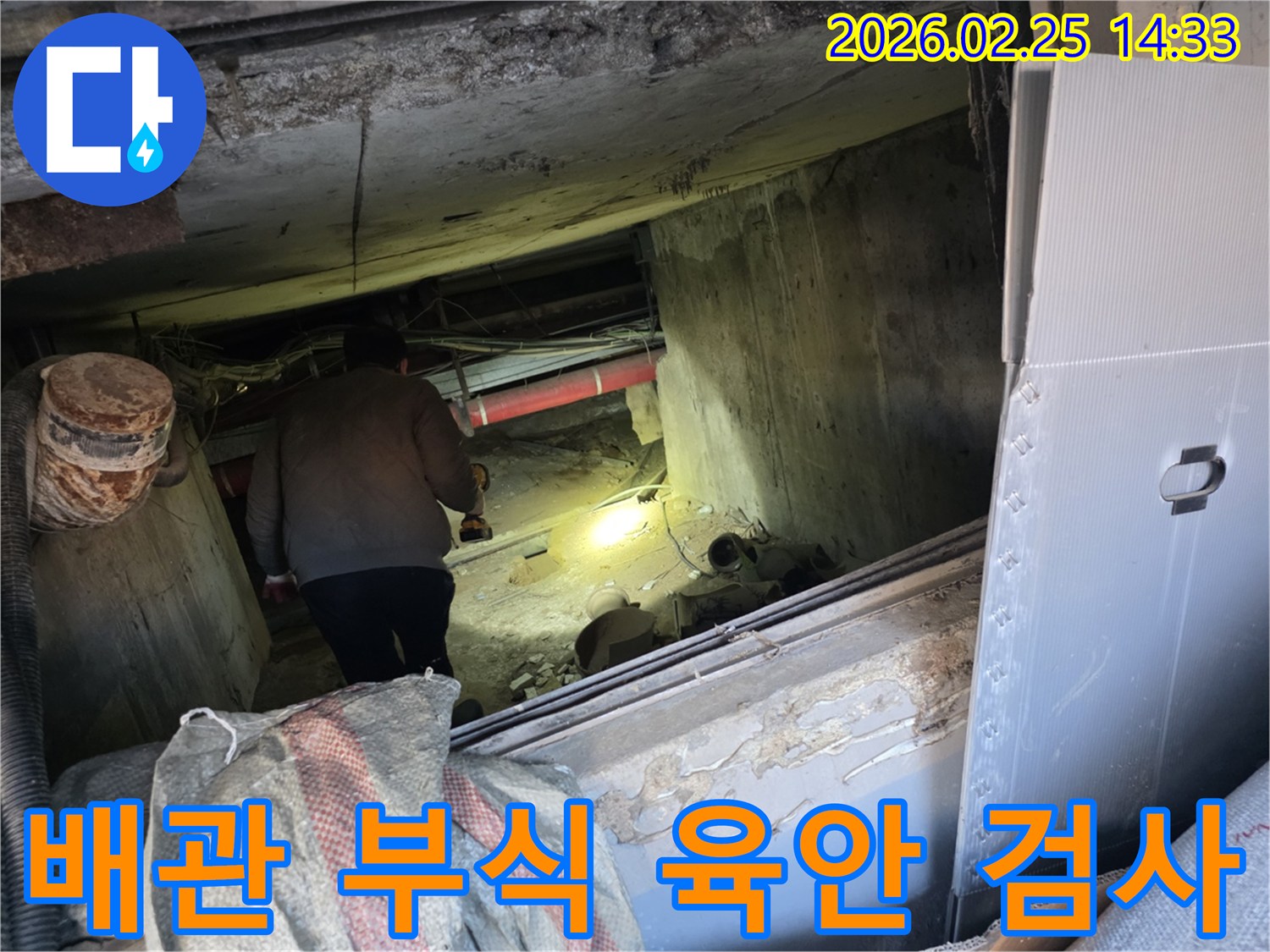누수 전문 엔지니어가-어둡고 좁은 공간에서-손전등을 비춰가며-배관의 부식 여부를-육안으로 꼼꼼히-검사하는 모습입니다.