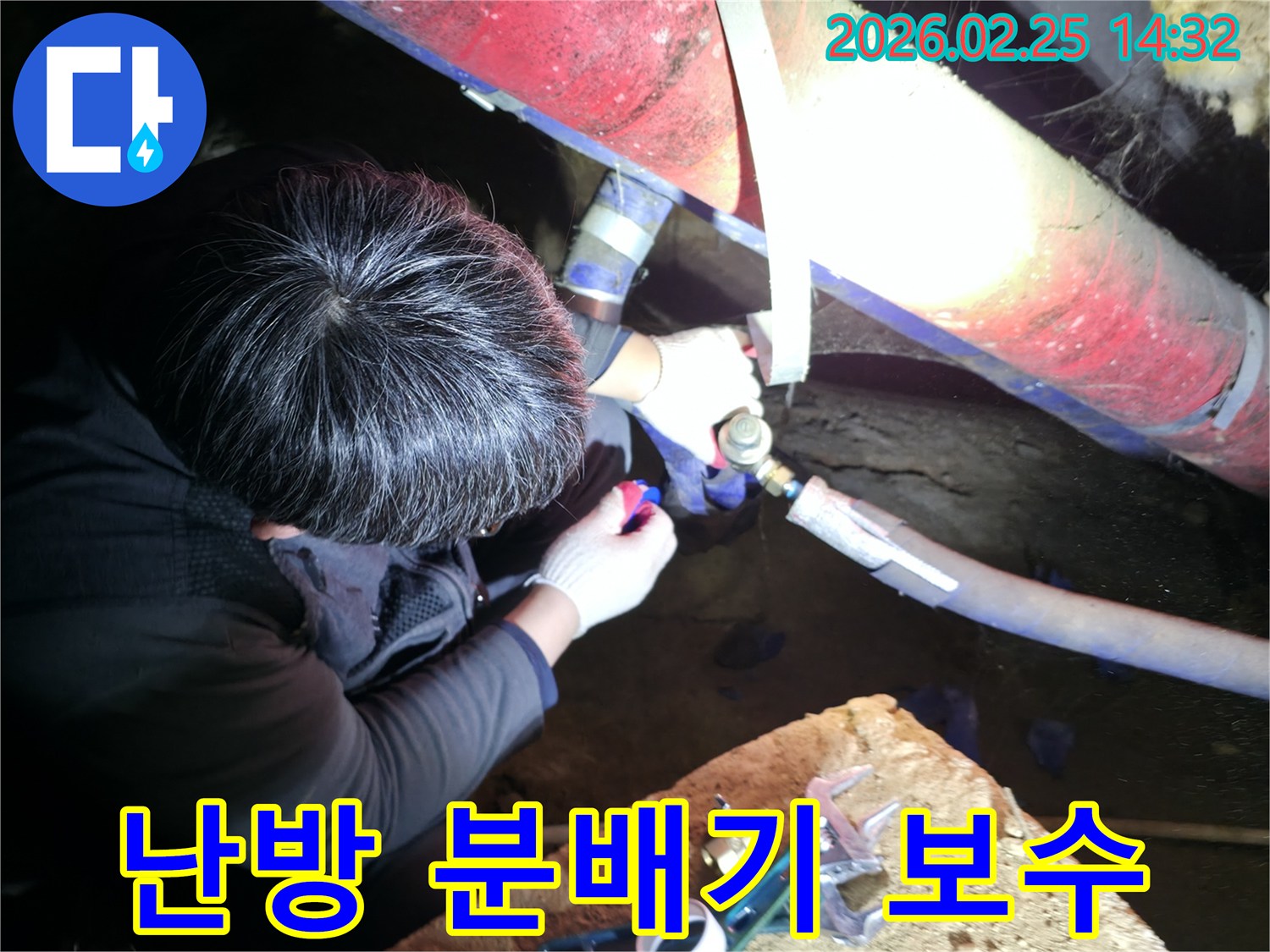 숙련된 누수 기술자가 좁은 공간에서 손전등을 비추며 난방관-분배기 연결 부위를 정밀하게 점검하고-수리하고 있습니다-난방누수해결-전문가수리