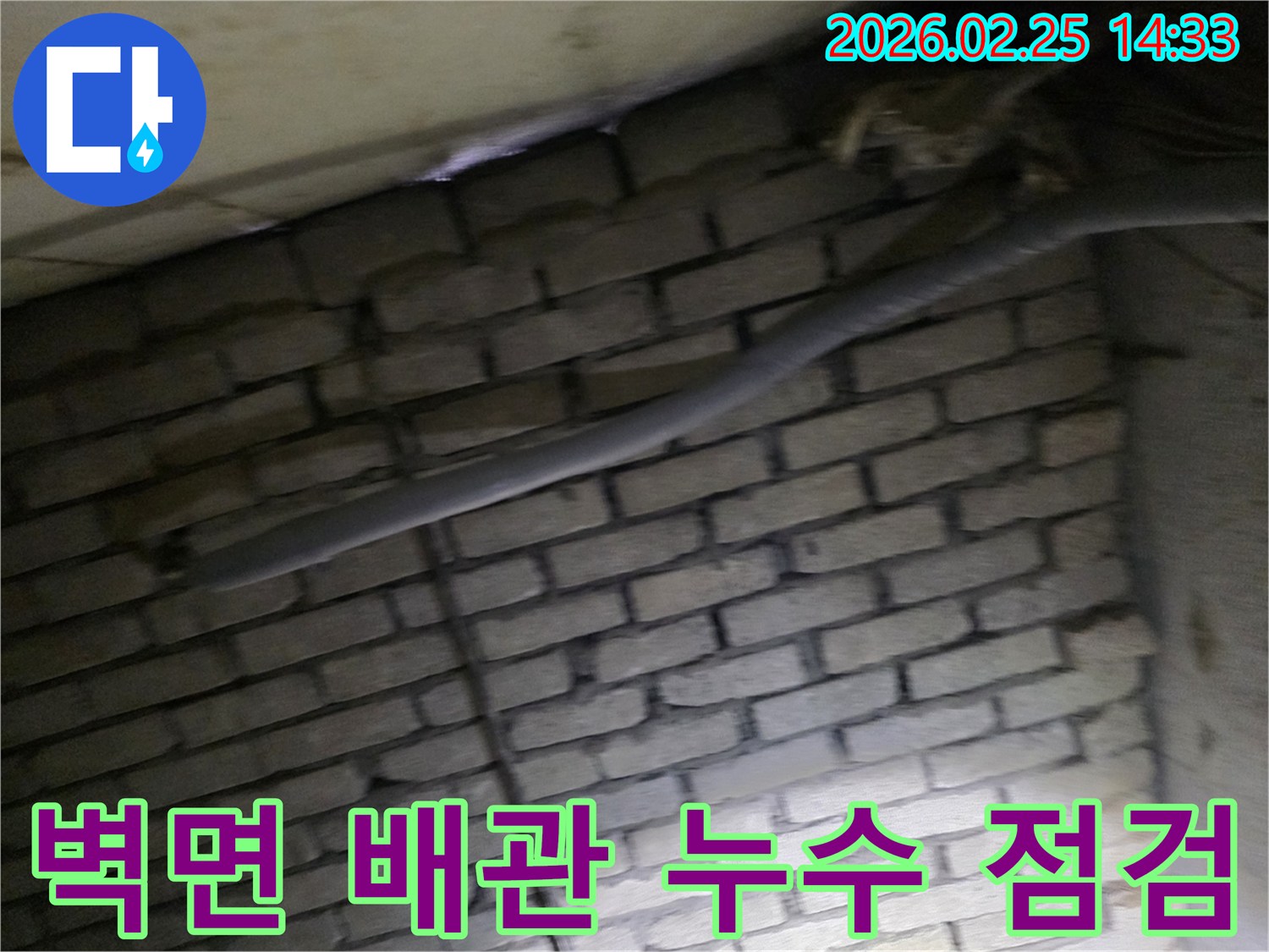 어두운 공간에서 벽돌 벽과 함께 보이는-단열된 배관과 다른 배선이-누수 점검을 위해 촬영된 이미지입니다.