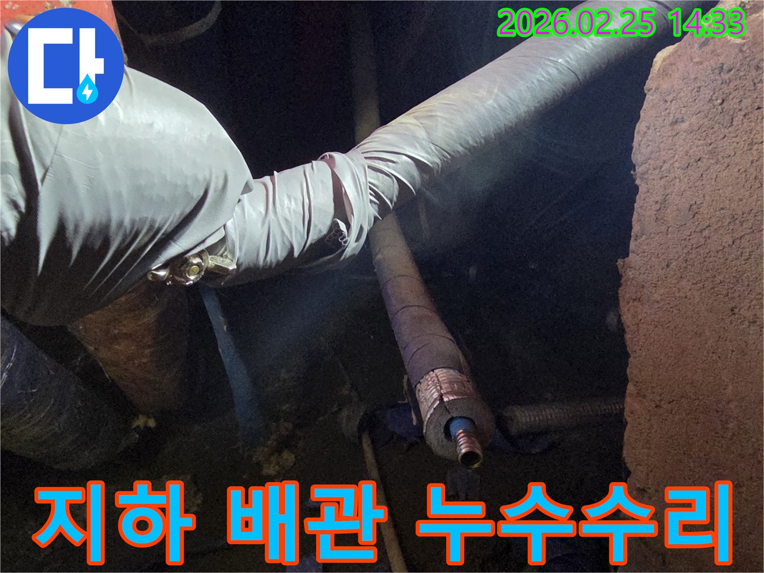 어둡고 좁은 지하 공간에서-장갑을 낀 손이-손상된 배관을-세심하게 점검하고-수리 준비를 하는-전문가의 모습입니다