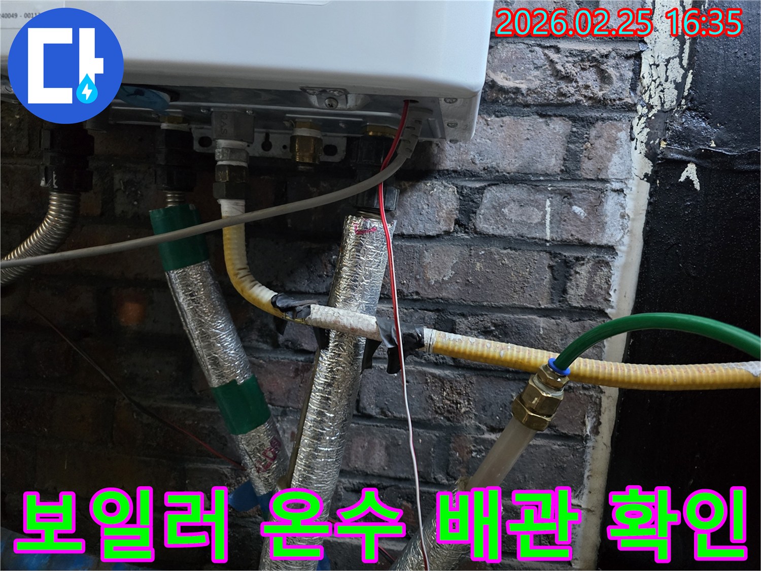이 이미지는-벽에 부착된-보일러 하단부의-온수 배관과-난방 배관-그리고-전선이-연결된-모습을-보여주며-일부 배관은-단열재로-감싸져 있습니다.