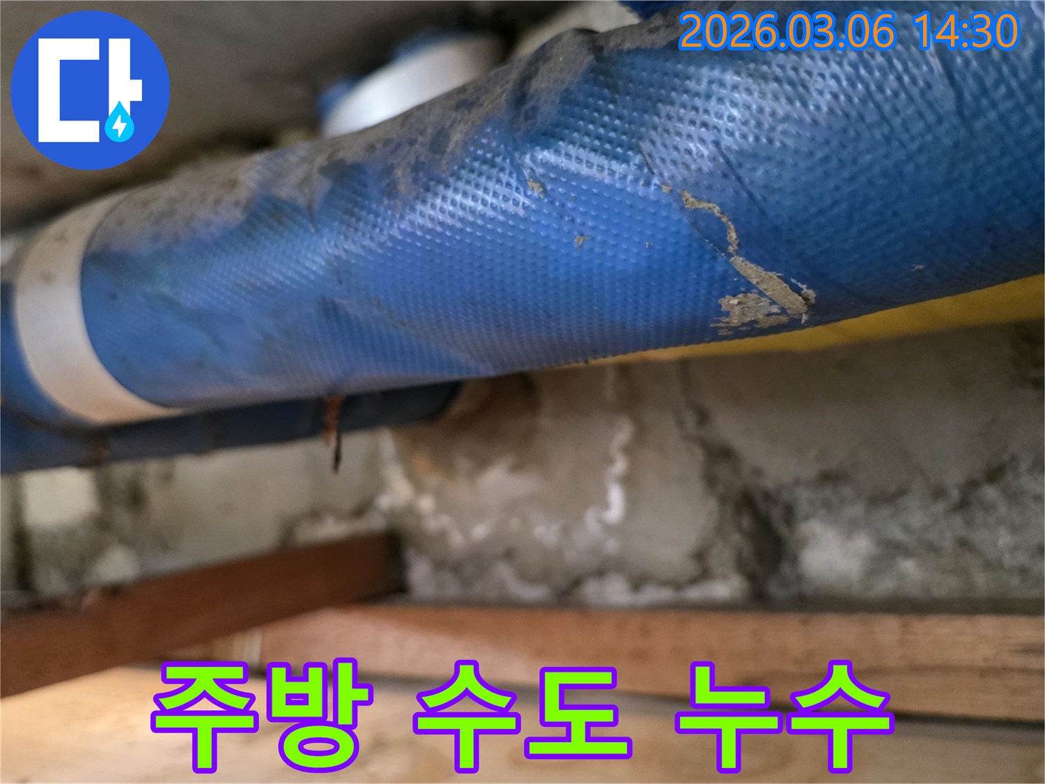 빌라 주방 하부-파란색 수도 배관과-젖은 콘크리트 벽면-그리고 나무 지지대를-꼼꼼히 점검하는 모습