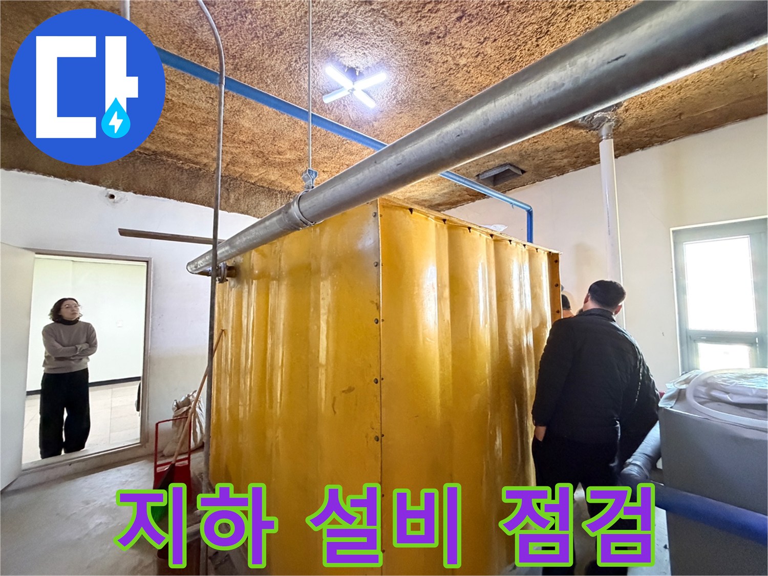 노란색 탱크 주변의 금속 배관과 천장 구조물을 촬영한 사진입니다.