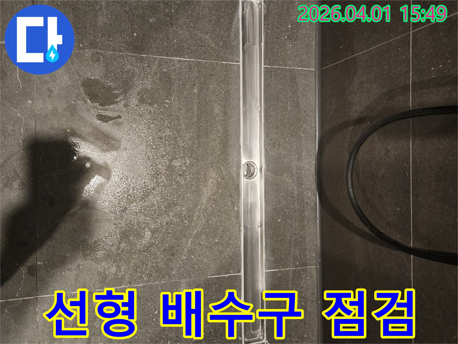 어두운 색상의 타일 바닥에 설치된 길고 얇은 샤워 배수구-주변에 물방울이 튀어 있습니다