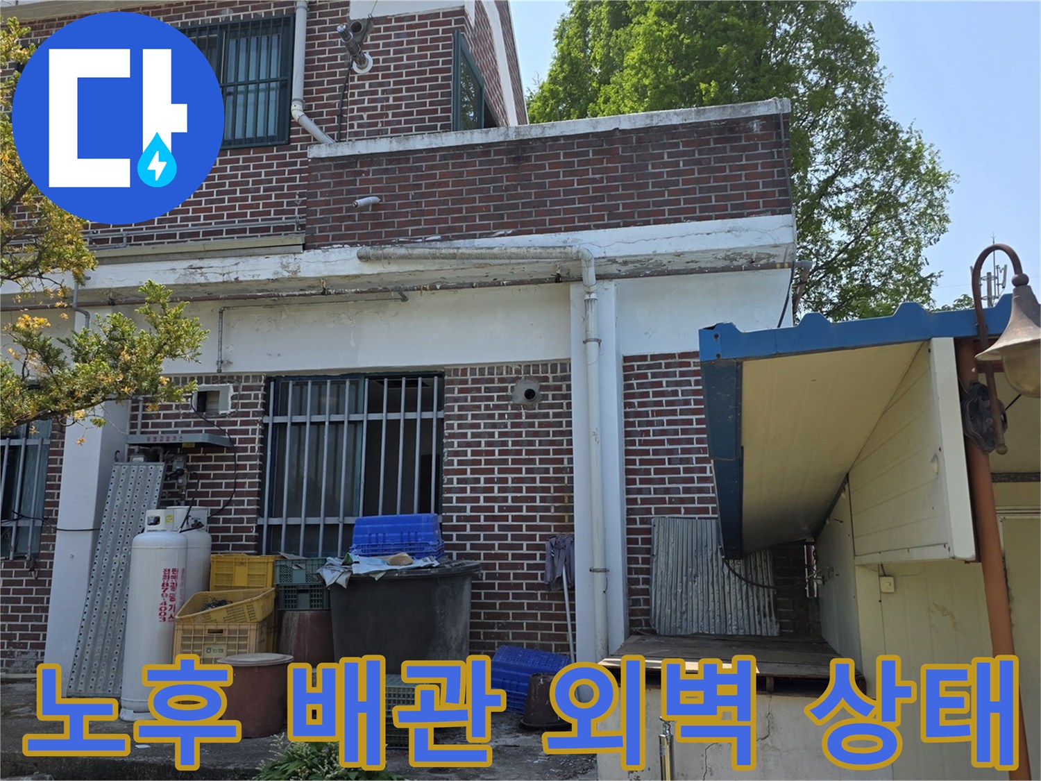 벽돌 외벽 아래쪽의 외부 수도 부속과 배관 연결 지점 사진입니다.