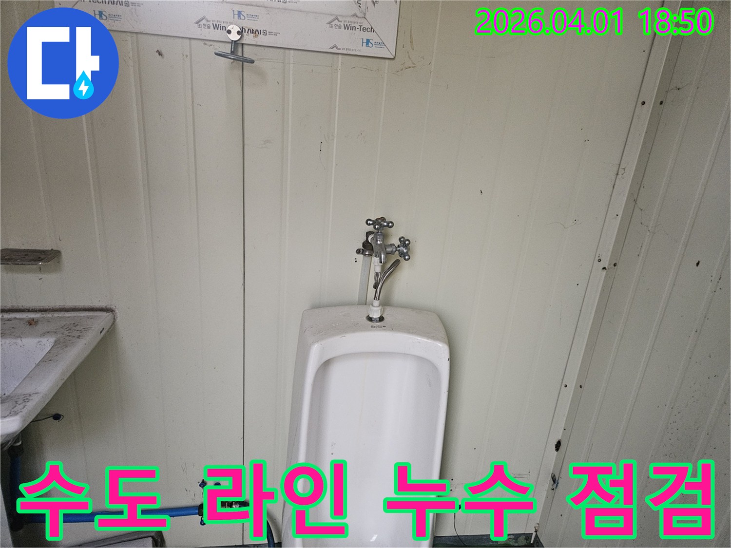 가설 화장실 소변기 주변의-전체 수도 라인-즉 수도꼭지, 급수 호스, 밸브 등을-종합적으로 점검하여 누수를 확인하는 모습