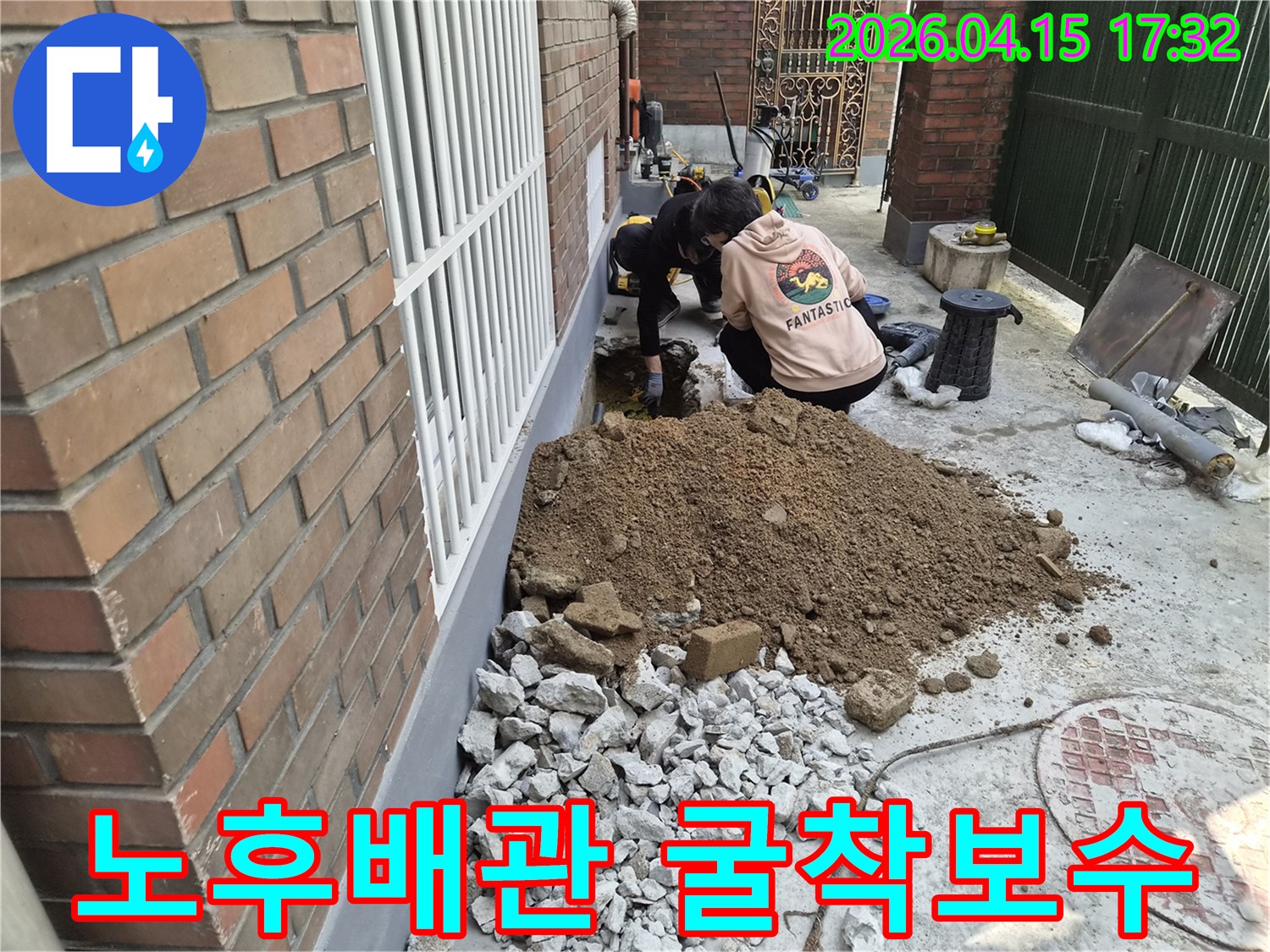 두 명의 작업자가-건물 옆에서-오래된 배관의 누수를 찾아-땅을 파내고 있는 모습