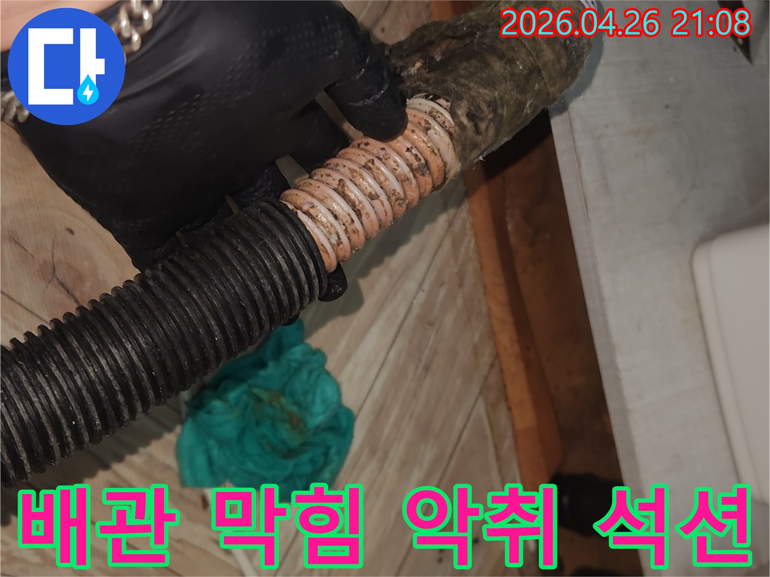 검은 장갑을 착용한 엔지니어가-오염된 싱크대 배수 호스를-석션 장비로 깨끗하게 청소하여-막힘과 악취를 동시에 해결하는 모습