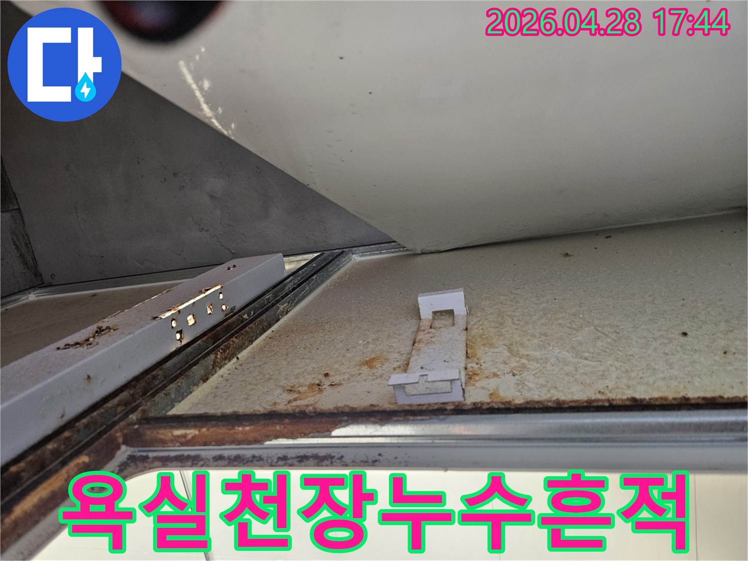 아래층 욕실 천장에서 발견된 심각한 누수 흔적을 보여주는 사진입니다-녹슨 금속 구조물과 변색된 천장 마감재가 명확하게 보입니다.