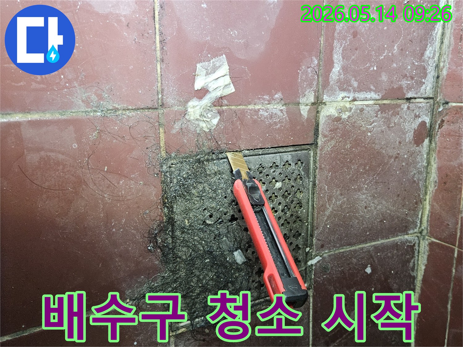 오래된 욕실 배수구에 엉킨 머리카락과 슬러지를 커터칼로 긁어내며 청소하는 모습-누수 예방을 위한 작업