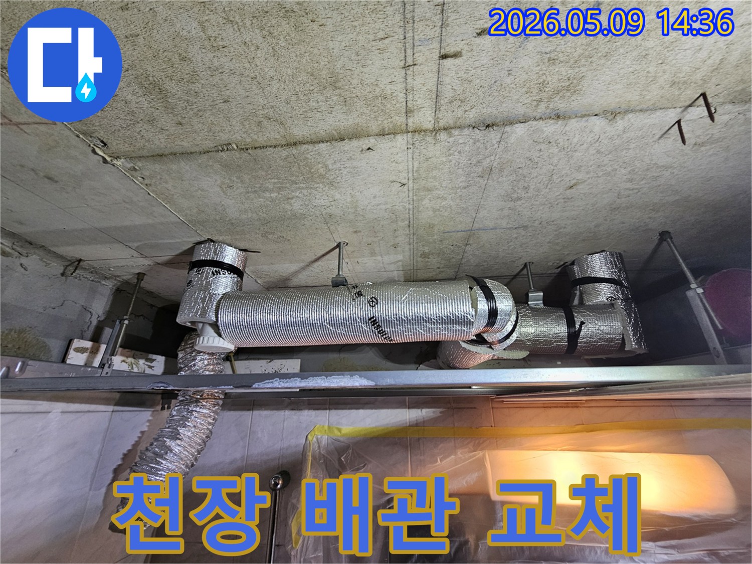 천장 콘크리트 구조물 아래에 설치된-기존 배관을 철거하고 새로운 배관으로 교체하는 공사 현장 사진입니다.