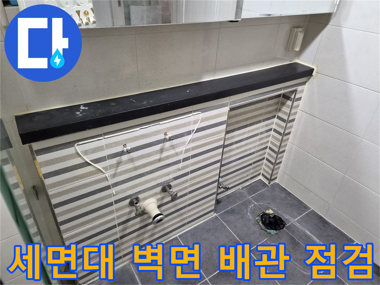 줄무늬 타일 벽면에 위치한 세면대용 수도 밸브와 연결 배관
