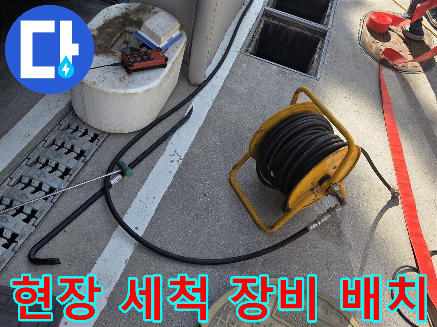맨홀 뚜껑 옆에 놓인 고압 호스 릴과 작업 도구들