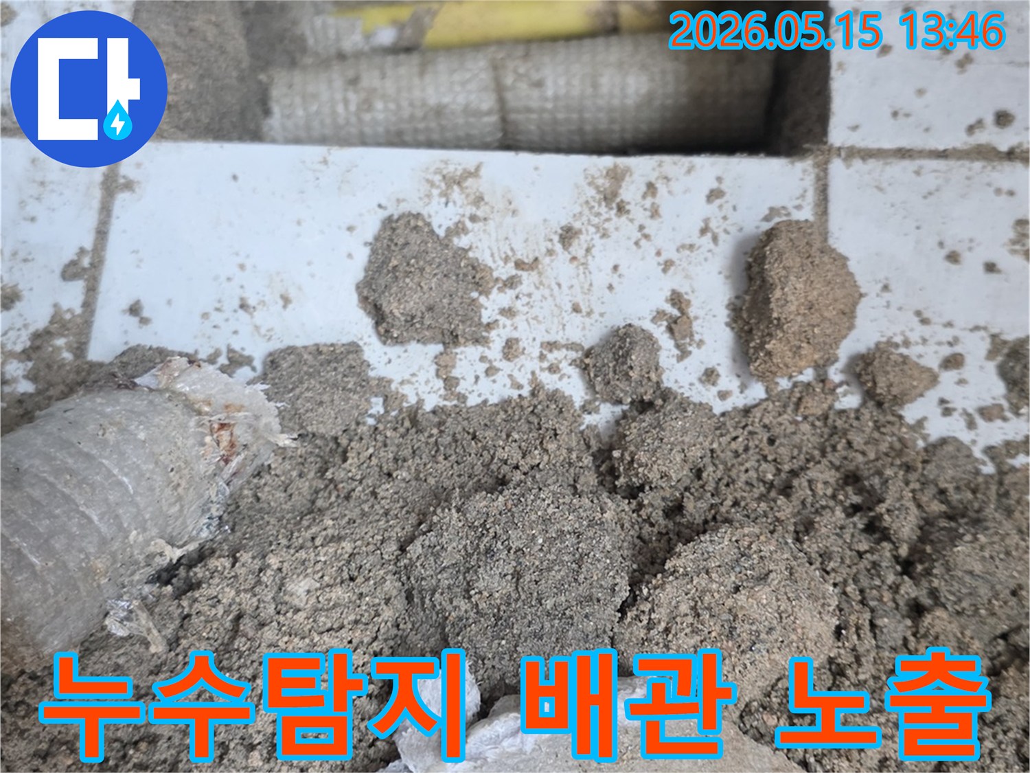 누수 공사 현장에서-바닥을 개방하여-드러난 배관과-주변의 흙더미-그리고-파손된 타일 조각들입니다