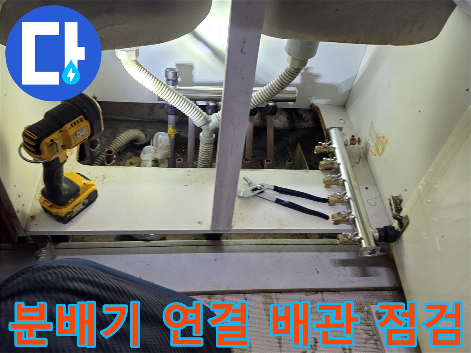 싱크대 하부의 보일러 분배기와 연결된 밸브 및 호스들의 근접 촬영 사진입니다