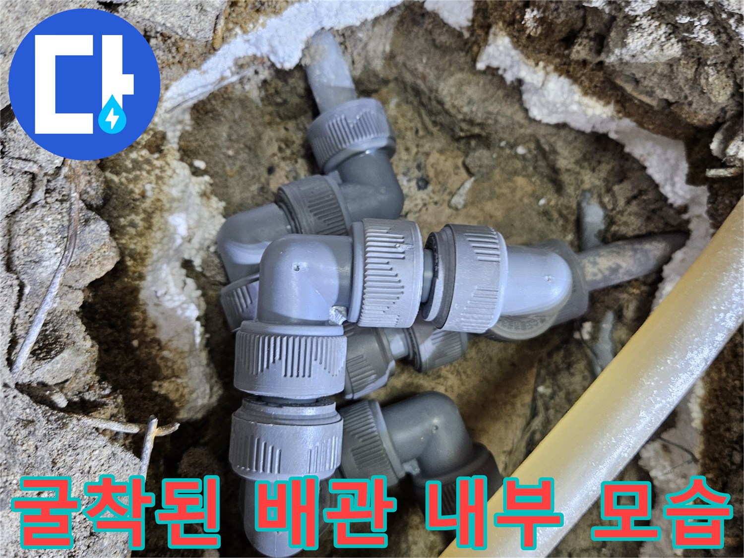 바닥 흙과 시멘트 사이로 드러난 수도 배관 연결부 사진입니다.