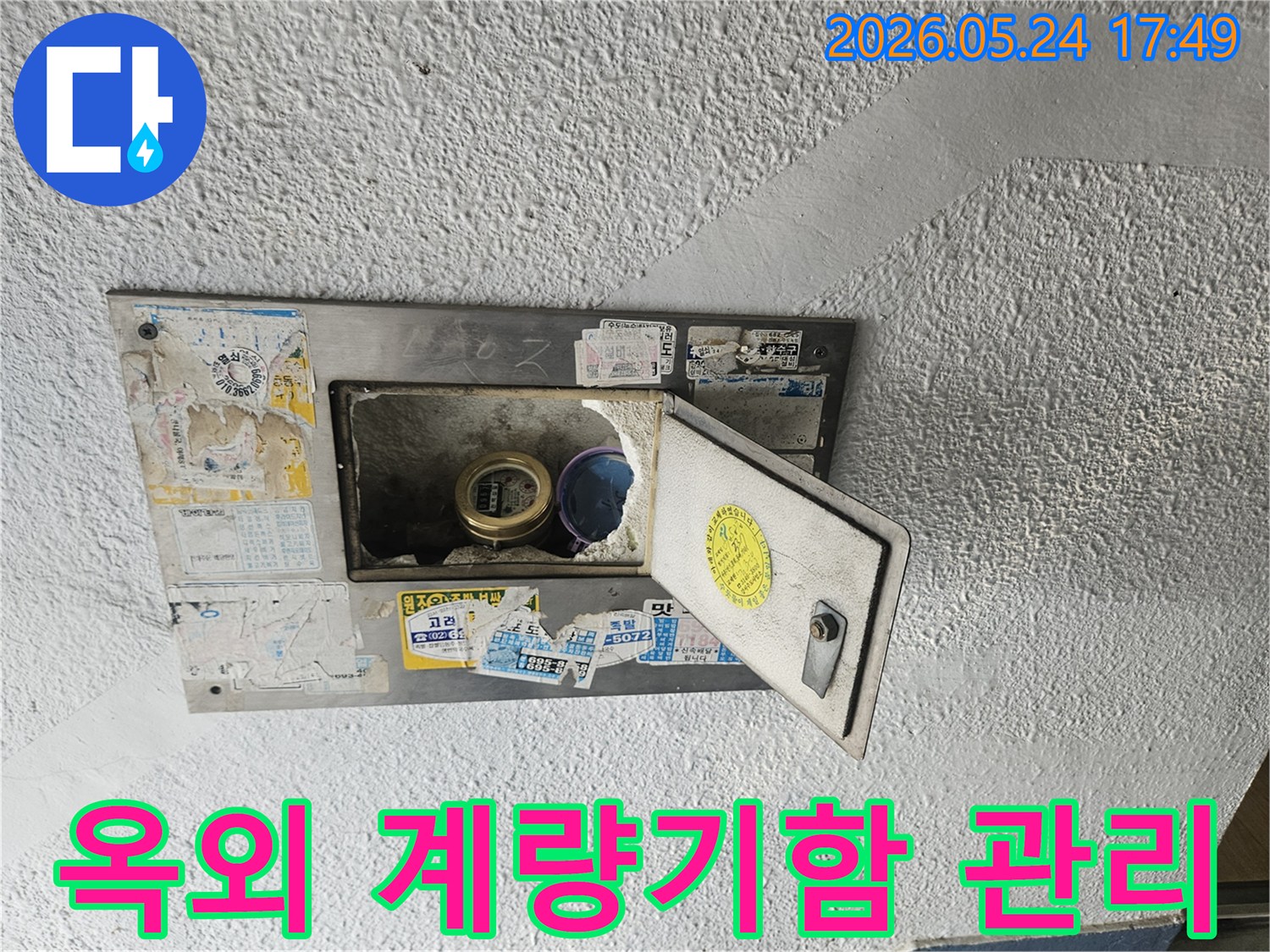 오래된 옥외 수도계량기함이 열려있고-내부 상태를 점검하며-누수 예방의 중요성을 보여주는 사진입니다.