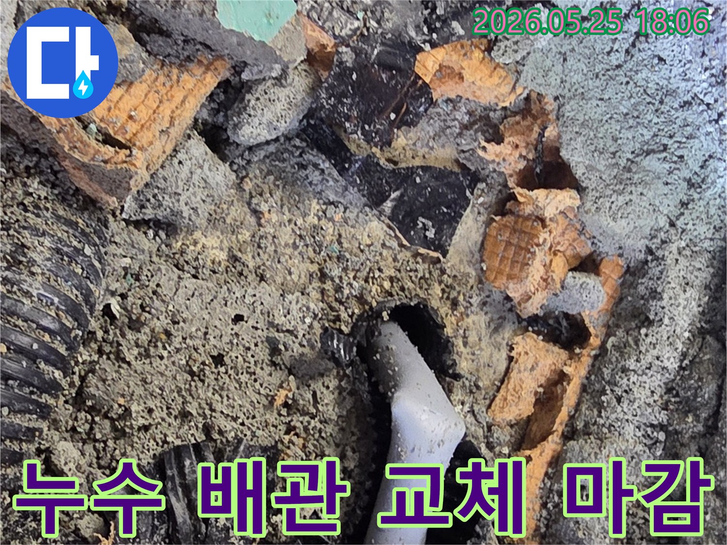 파쇄된 바닥 아래에서 드러난 젖은 배관과 주변의 흙-콘크리트 조각들은-누수 수리를 위한 배관 교체 작업을 보여줍니다.