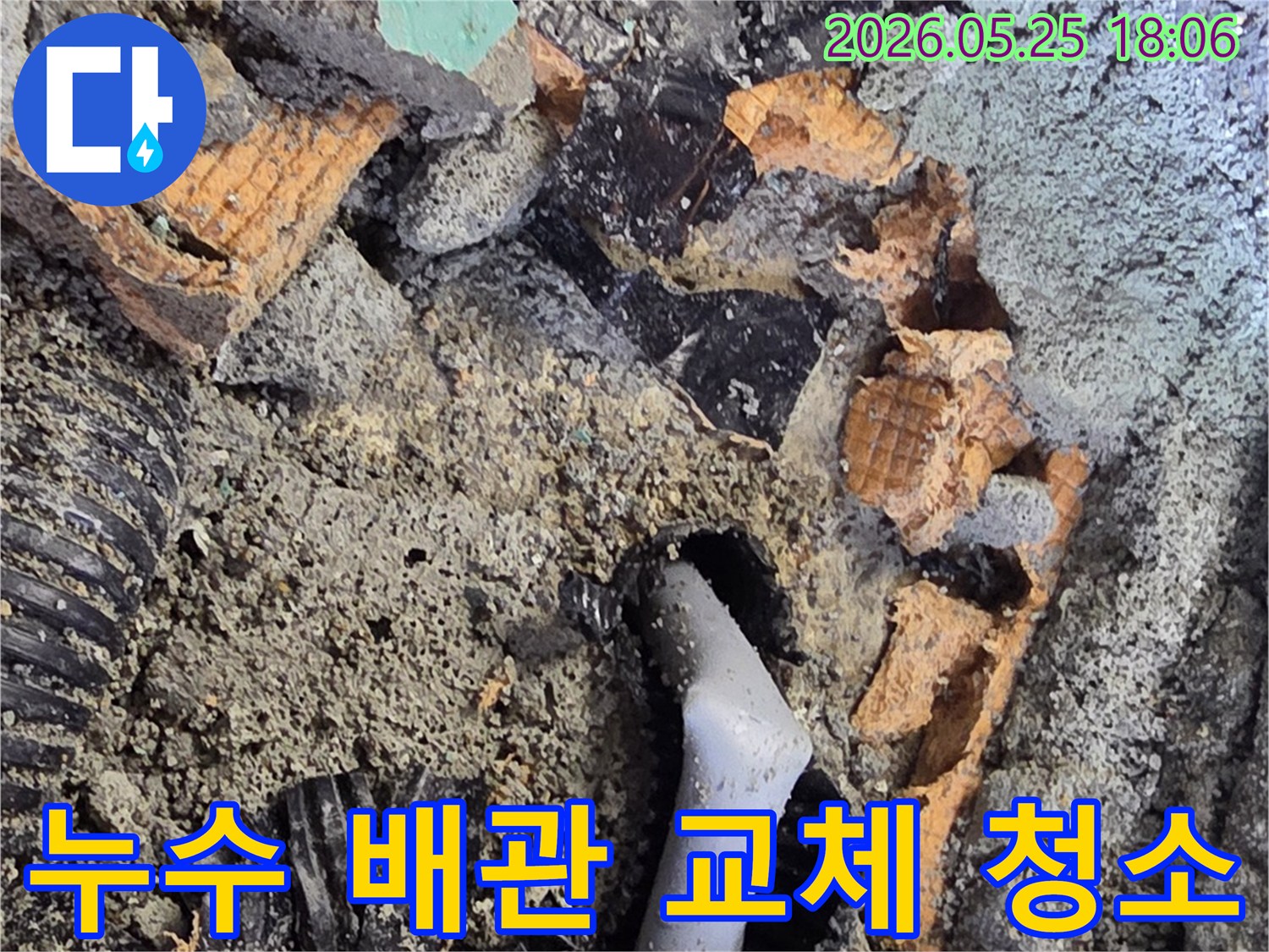 파쇄된 바닥 아래에서 드러난 젖은 배관과 주변의 흙-콘크리트 조각들은-누수 수리를 위한 배관 교체 작업을 보여줍니다.