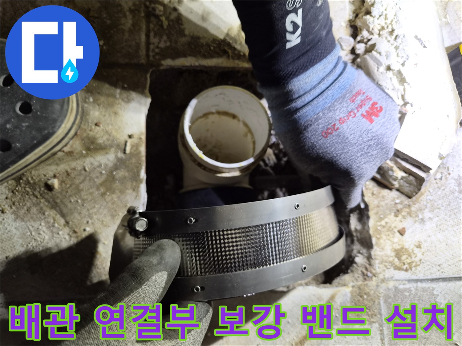 누수가 발생한 배관 연결 부위에 금속 보강 밴드를 적용하는 장면입니다.