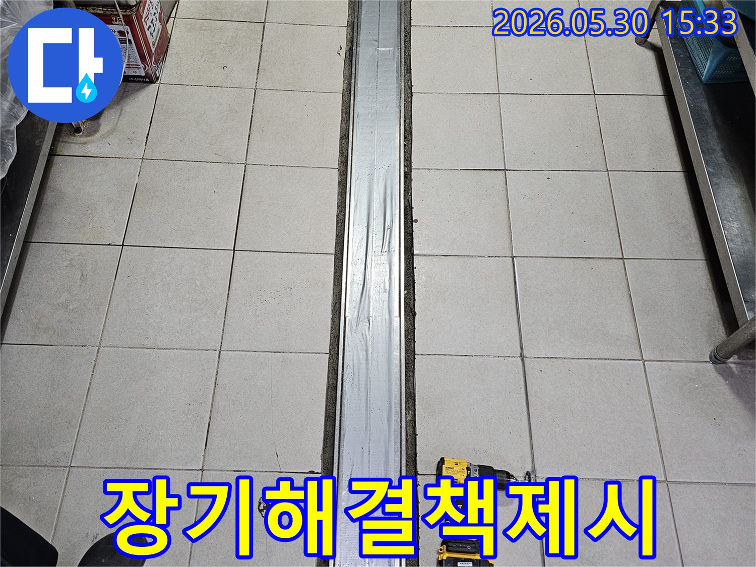 타일 바닥과-배수 트렌치-그리고 작업용 전동 드릴이 놓인-장기적인 해결책을 위한-누수 보수-준비 현장입니다