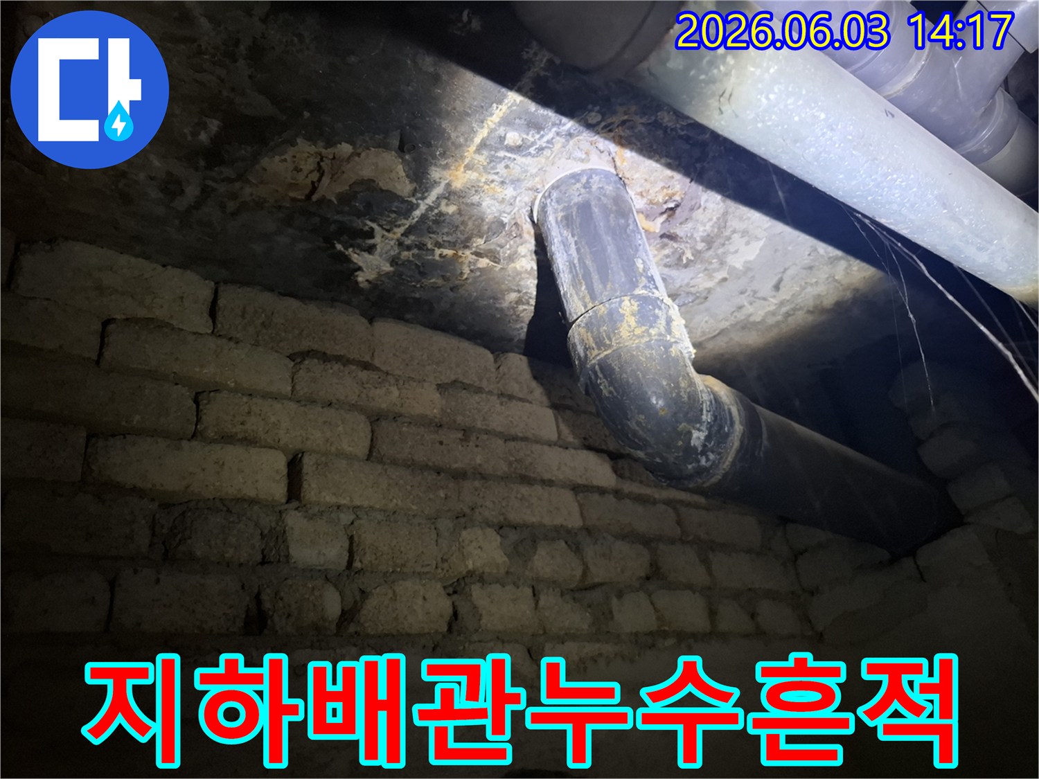어두운 지하 공간에서-낡은 배관과-벽돌 벽에 발생한-누수 흔적을-조명으로 비춰-면밀히 조사하는 모습