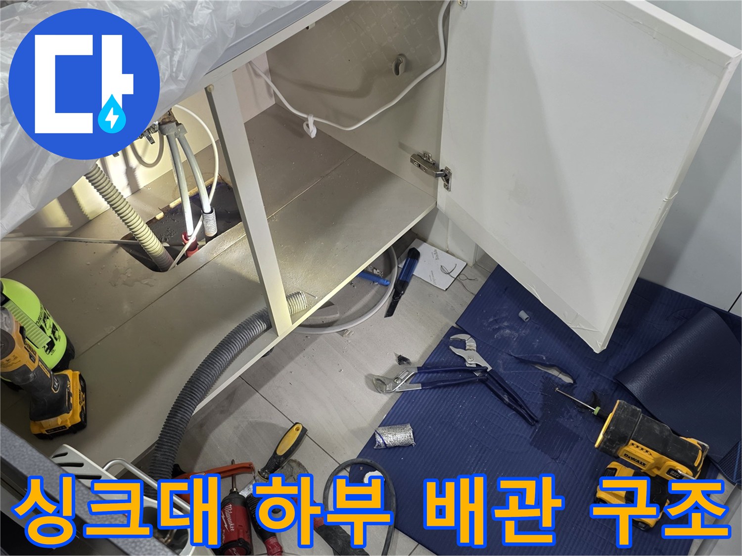 싱크대 아래 공간의 PVC 관과 작업 도구들이 놓여있는 장면