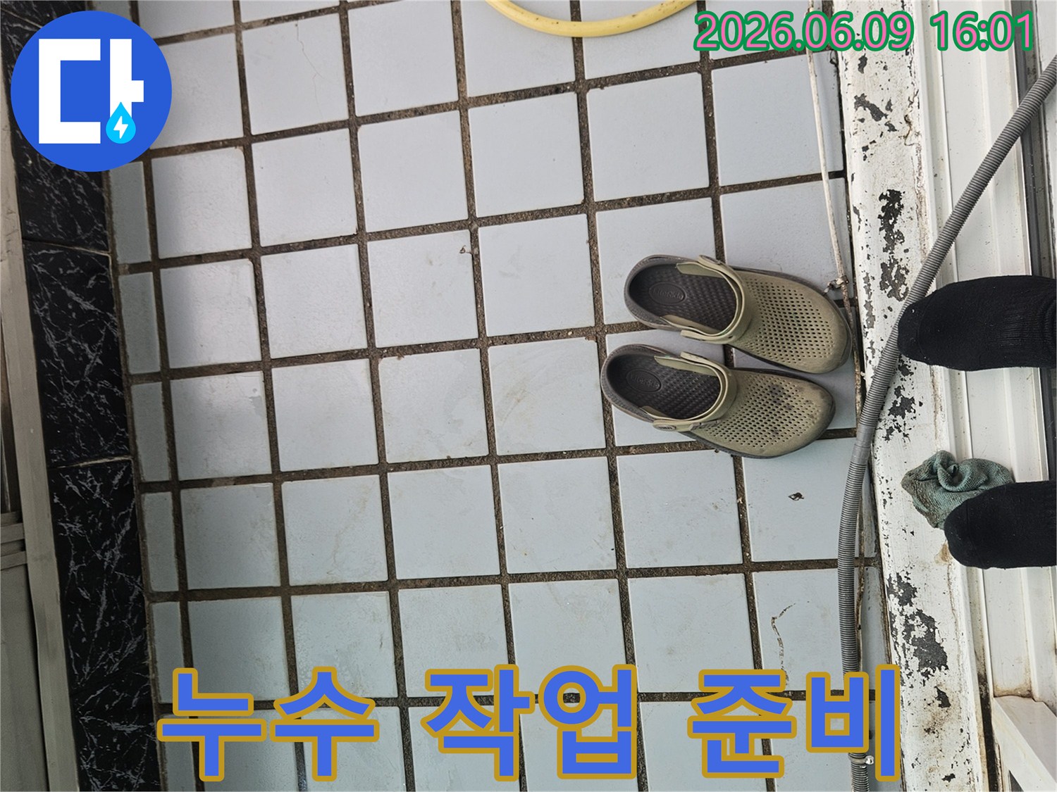 누수-현장의-타일-바닥과-함께-작업화와-호스가-놓여있는-모습으로-작업-준비-상황을-보여줍니다.