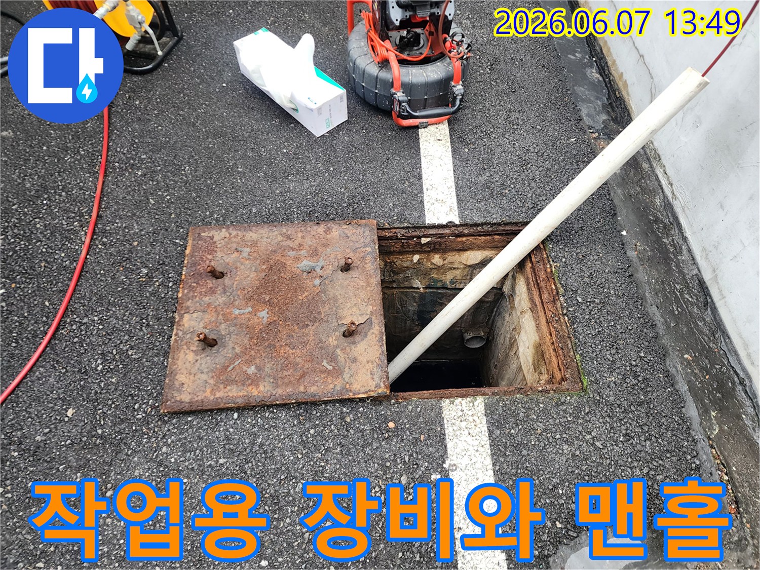 맨홀 입구에 배치된-배관 점검용 장비와 흰색 파이프