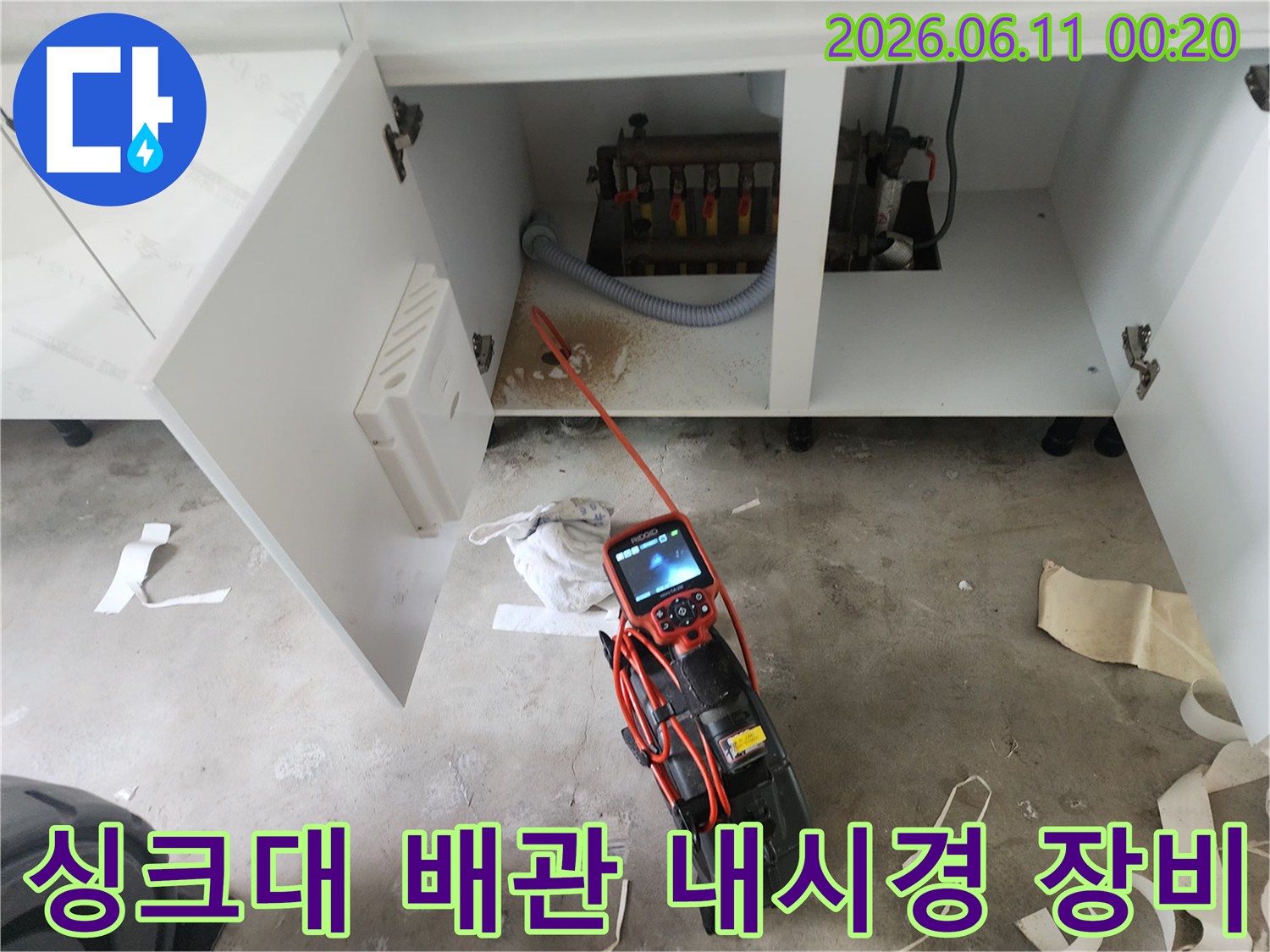 싱크대 밑 공간에서 작동 중인 배관 내부 검사용 내시경 화면과 본체입니다.