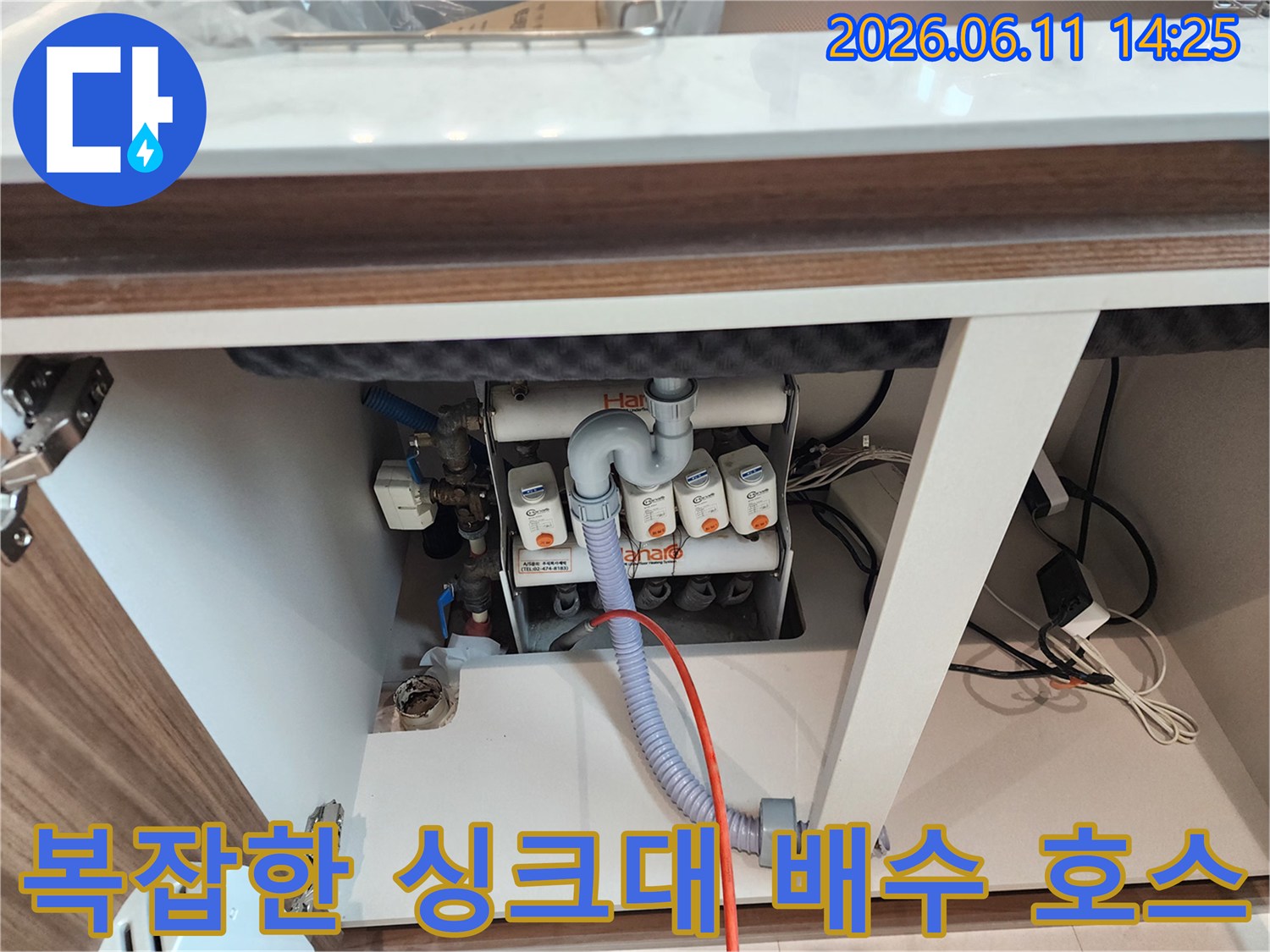 싱크대 하부장 내부의 화이트 톤 분기 배관과 연결된 유연한 배수 호스 모습
