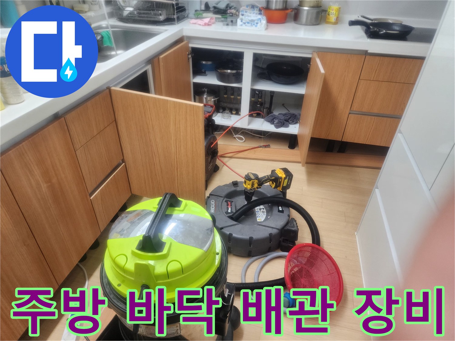 주방 싱크대 아래 배치된 배관 청소용 진공 흡입기와 작업 도구들