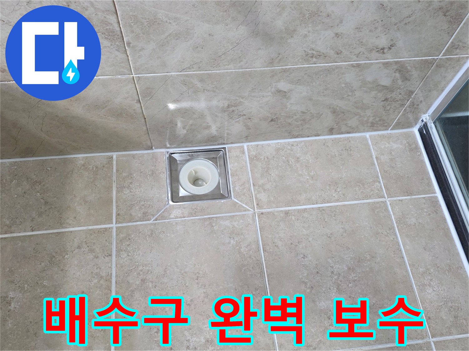 베이지색 타일 바닥에 설치된-금속 사각 배수구의 모습으로-주변 타일과 줄눈의 마감 상태를 보여줍니다