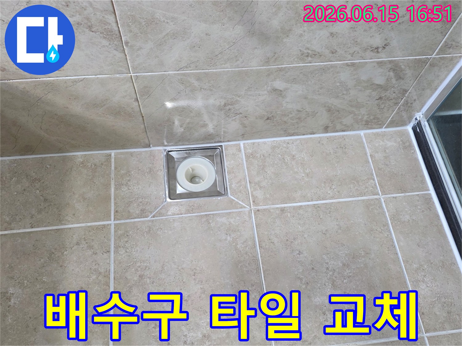 베이지색 타일 바닥에 위치한-사각형 금속 배수구의 모습으로-주변 타일의 접합부와-줄눈의 상태를 상세히 보여줍니다