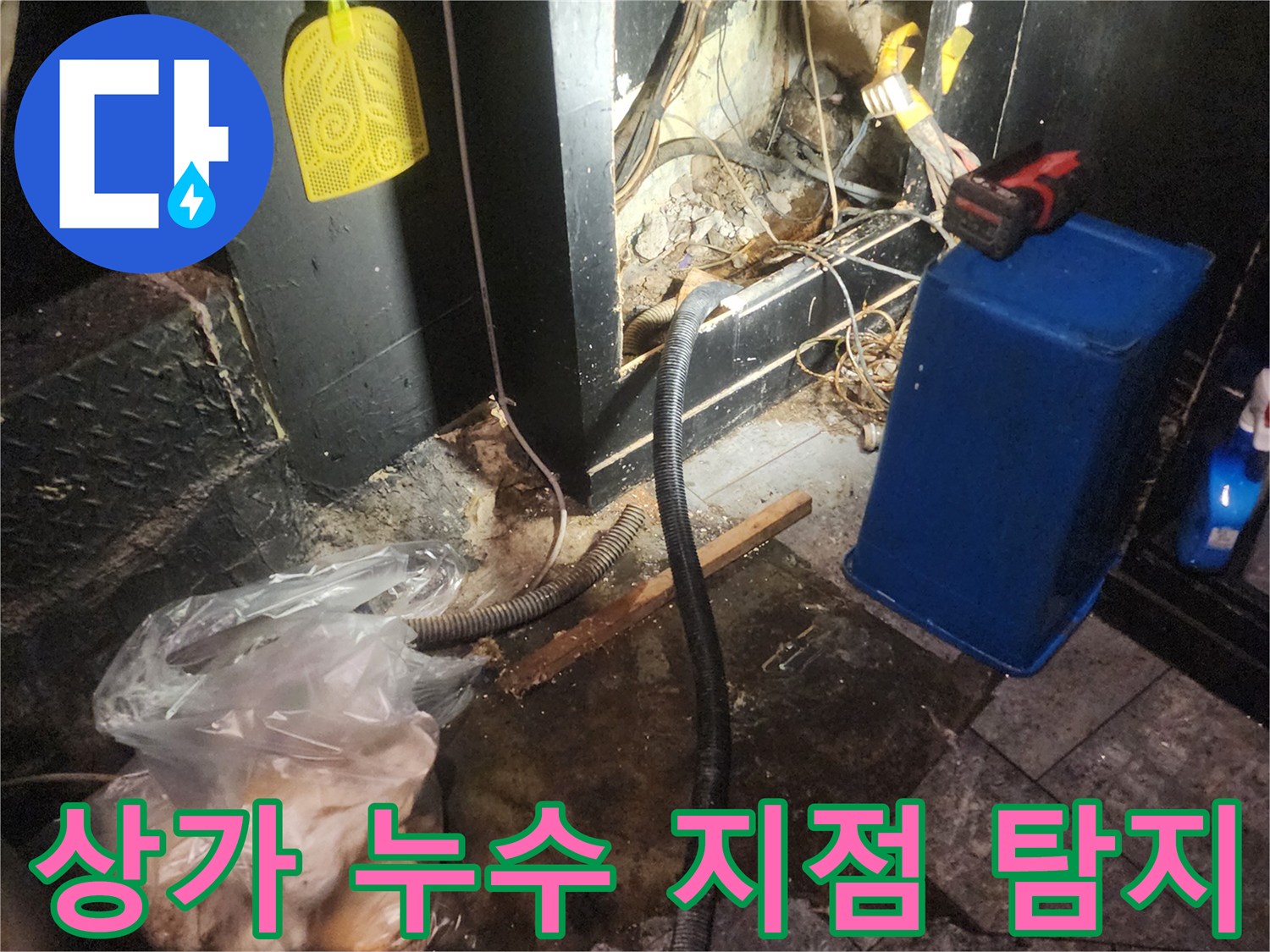 어두운 상가 바닥 아래에서 복잡하게 얽힌 배관과 전선-그리고 물이 새는 흔적을 보여주며 누수 발생 지점을 정밀 탐지하는 현장 이미지
