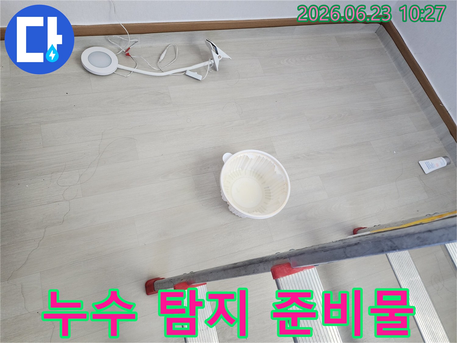 천장에서 떨어지는 물을 임시로 받는 그릇과-누수 지점 확인을 위한 사다리-정밀 탐지를 위한 조명 장비가 바닥에 놓여 있는-누수 공사 전 준비 모습입니다