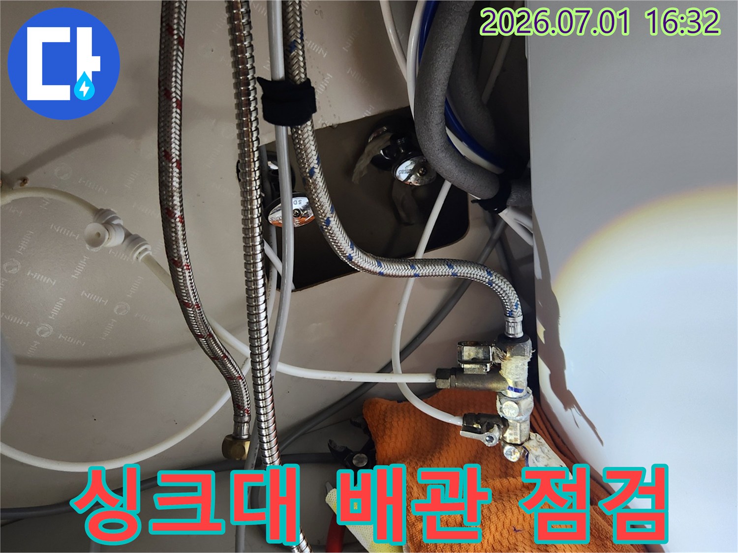 이 사진은-싱크대 하부의-복잡한 배관과-수전 연결부를-점검하는-전문가의 모습을 담고 있습니다